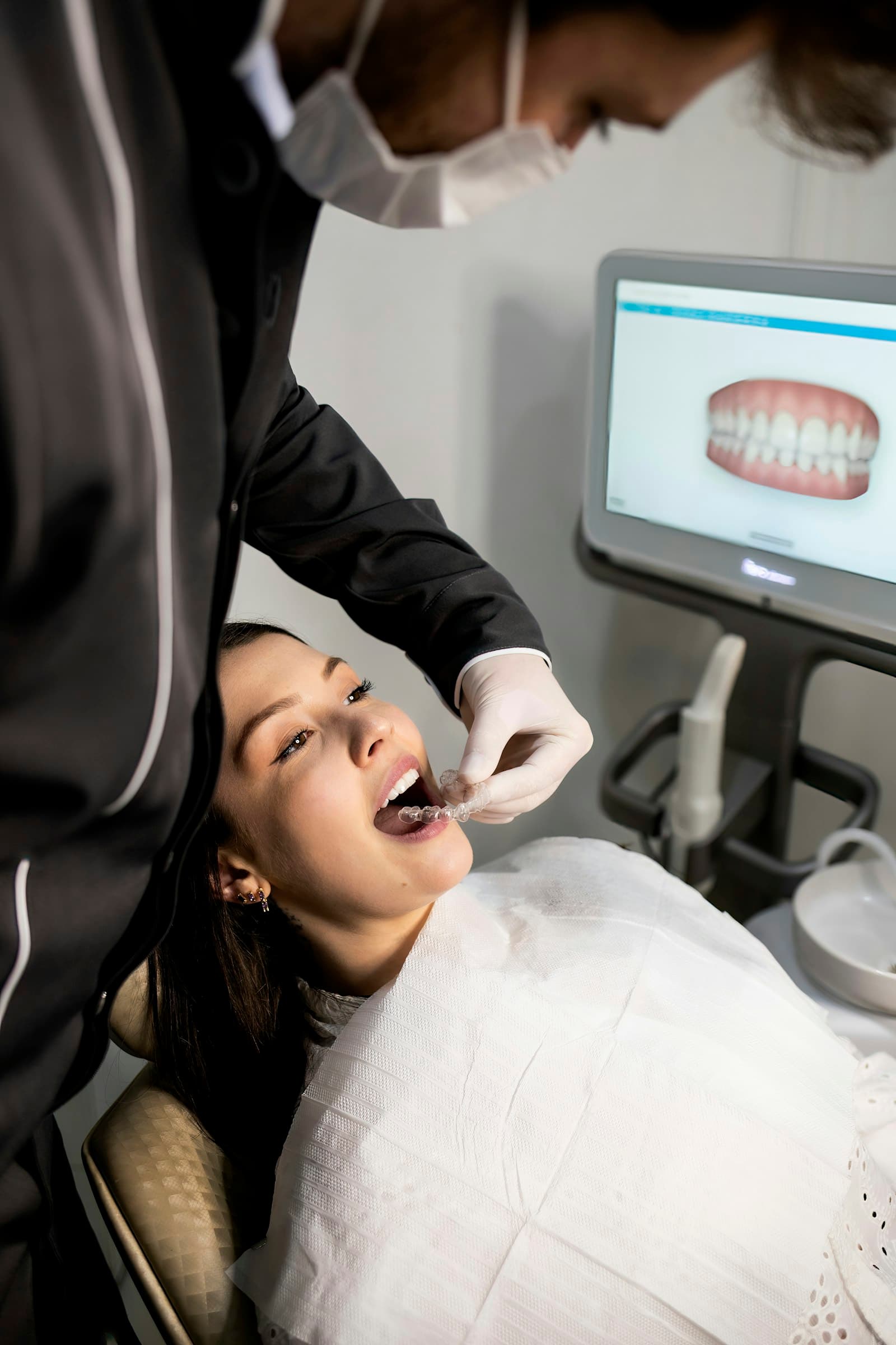 A dentist fitting a clear aligner with a digital scan on screen